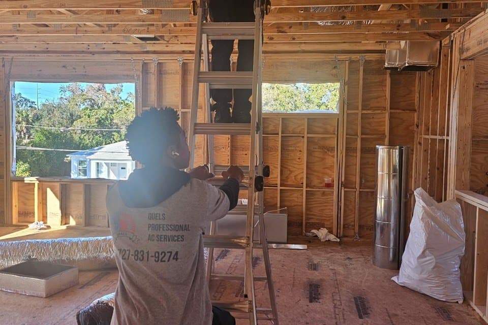 A Quel's technician on a step ladder running duct in a house still at the framing stage.