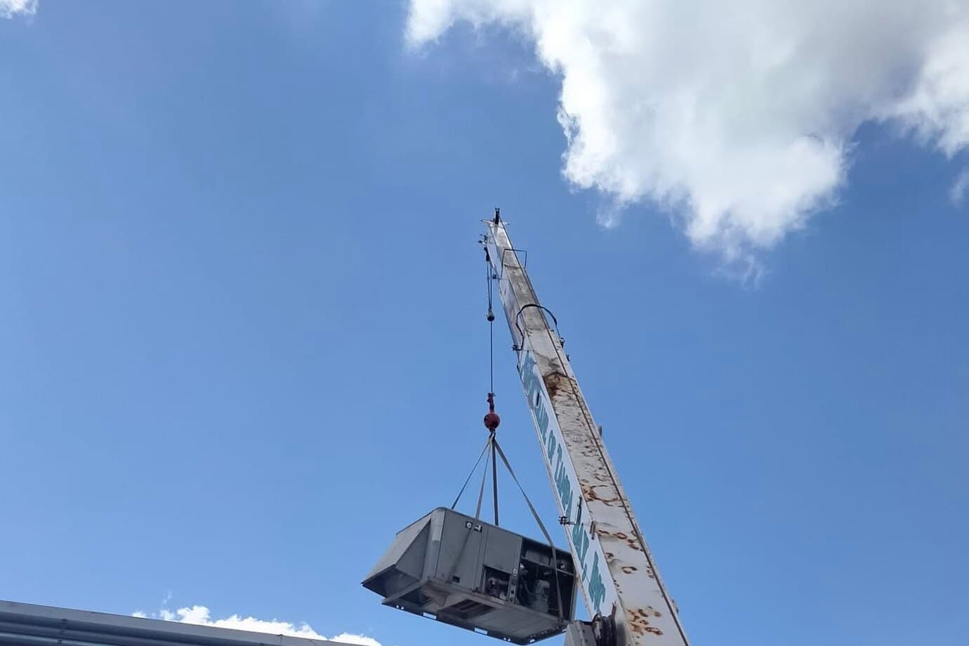 A crane lifting a rooftop package air conditioning unit over the roof of a commercial building.